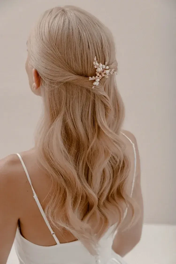 A person with long, wavy blonde hair styled in a half-updo, adorned with a decorative hairpiece. They are facing away from the camera.